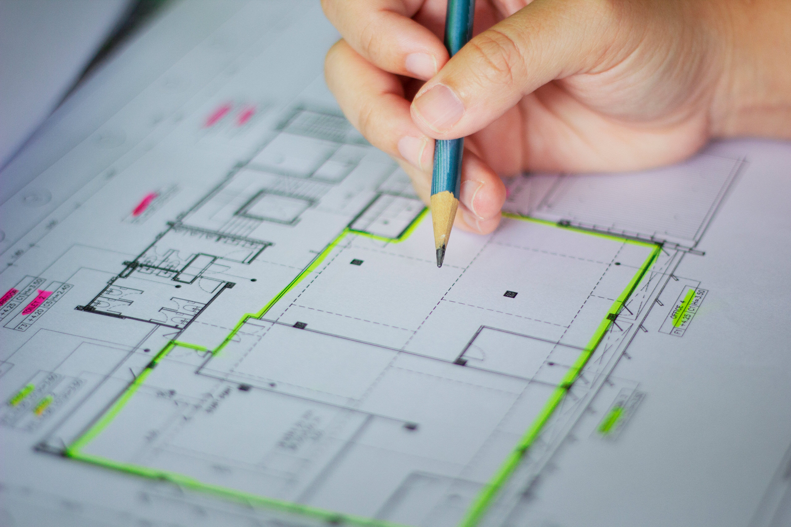 Gros plan sur une main annotant au crayon un plan d'architecture surligné en vert et rose