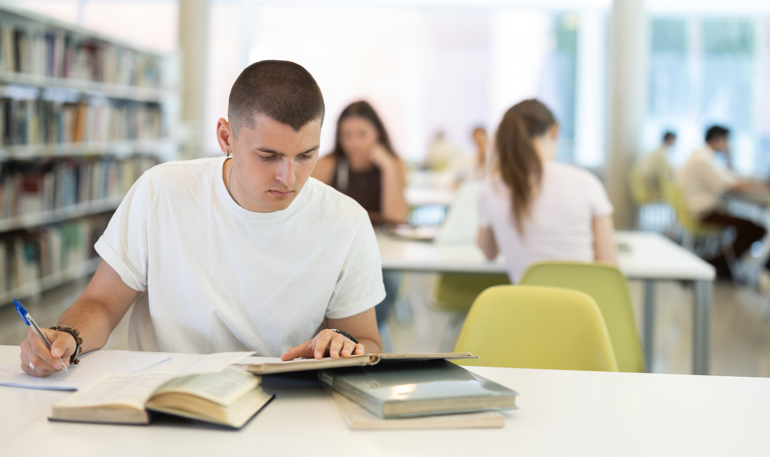Jeune homme étudiant prenant des notes à son bureau en classe, d'autres élèves travaillant en arrière-plan